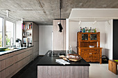 Old dresser in modern kitchen with grey fronts and concrete ceiling