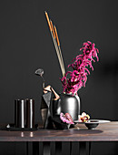 Black vase of pink Amaranthus on table in front of black wall