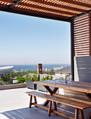 Wooden table and bench on roofed terrace with sea view