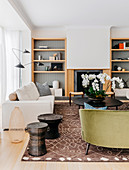 Upholstered furniture, side tables, floor vase and coffee table in front of built-in fireplace, flanked by open wooden shelves
