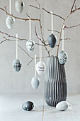 Easter eggs hand-painted in shades of grey hanging from twigs