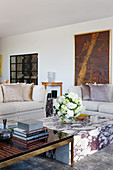 Books on ebony and brass coffee table, marble coffee table with bouquet of flowers, elegant sofa set in background