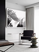 Upholstered chair and designer side table in front of black and white picture on the wall