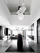 Designer-Pendelleuchte über rundem Tisch mit Orchidee in offenem Wohnraum mit doppelter Raumhöhe