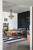 Round table and rattan chairs below chandelier and sofa against wall painted with chalkboard paint