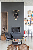 Cowhide rug, side table and black chair in front of bull's head on black wall above fireplace