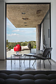 Elegant chair, footstool and side table in front of glass wall with view onto terrace