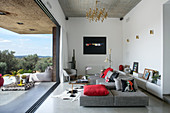Grey sofa set with red scatter cushions in living room opening onto terrace