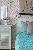 Mint-green bedside cabinet and bed against polka-dot wallpaper