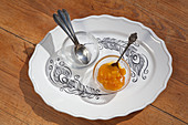 Bowls, spoons and jam on plate with feather pattern