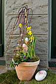 Potted pussy willow decorated with Easter eggs, narcissus and moss next to Easter egg by front door