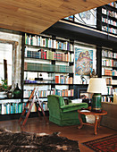 Lamp on antique table and green armchair in front of bookcase