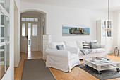 Sitzmöbel mit weißen Hussen, Paletten-Couchtisch und heller Holzdielenboden im Wohnzimmer, in umgebauter Molkerei