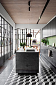 Black kitchen unit with green wall tiles and kitchen island, pizza oven on the terrace in the background