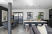 Kitchen island with barstools, dining table with grey upholstered chairs in open-plan interior