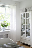 Linen in glass-fronted cabinet in bedroom decorated entirely in white