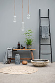 Black ladder and bathroom utensils on wooden bench against grey wall