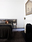 Bed with dark cover and gray headboard next to an open fireplace