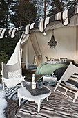 Camp chairs and round table on rug outside furnished tent decorated with fairy lights