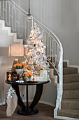 White Christmas tree and festive decorations on table at foot of staircase