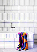 Wall-mounted bathtub and white wall tiles with blue joints in the bathroom