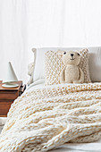 Crocheted teddy, knitted cushion and knitted blanket on bed