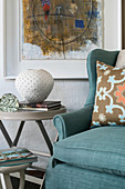 Turquoise armchair and side table below painting on wall