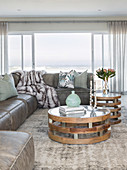 Two round coffee tables made of wood, glass and metal in front of leather sofa