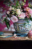 Rosa Blumenstrauss in Porzellanvase und Cupcake auf rustikalem Holztisch