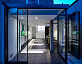 View into modern kitchen-dining room through open glass wall at twilight