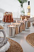 Alternativer Adventskranz. Vier Blechdosen mit Kerzen, im Hintergrund Eierlikörkuchen