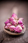 Dried rose buds on wooden spoon (close-up)