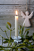 Christmas-tree candle on sprig of mistletoe in front of wooden angel