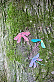 Gebastelte Libellen aus bemalten Ahornsamen an bemostem Baum
