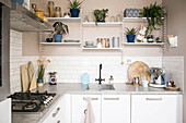 Utensils and houseplants on shelves on beige wall of L-shaped fitted kitchen