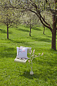 Romantic seat under flowering cherry tree: handmade cushion on chair next to branch wound with white yarn and decorated with crocheted flowers