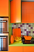 Orange kitchen cupboards with green worksurface and fitted appliances