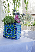 Blumen in einer Vase mit blau-grün gehäkelter Hülle