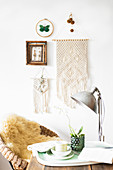 Macrame wall hanging on white wall with cup and flowers on tray in foreground