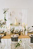 Table set for wedding with vase of tulips, dry twigs and pillar candles in front of wedding cake on sideboard