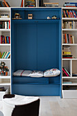 Cupboard repurposed as reading niche surrounded by bookcase