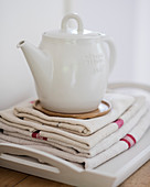 weiße Teekanne auf gefalteten Leinentüchern