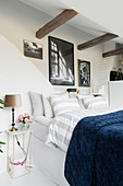Weißes Schlafzimmer mit Doppelbett, darüber rustikale Holzbalken