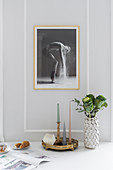 Arrangement of candles and vase on dining table below large photo on pale grey wall