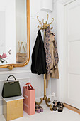 Brass coat stand and gilt-framed mirror in white hallway