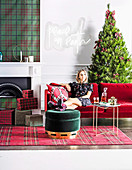 Blond woman sitting on red sofa in front of Christmas tree, in front of fireplace Christmas presents
