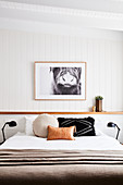 Scatter cushions on double bed in bedroom with white wood-panelled walls