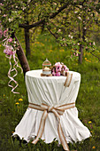 Ornate tablecloth, candle and peonies on round table below tree