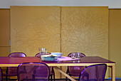 Dining table and purple acrylic chairs in front of sliding doors with relief decoration