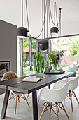 Wooden dining table and white shell chairs below pendant lamps